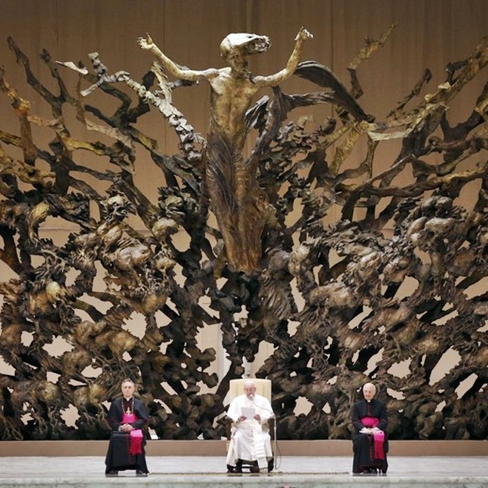 Pope Francis I sits under a wooden sculpture in the Paul VI general audience hall during an audience for members of the media, at the Vatican