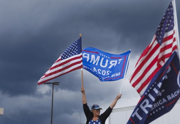 epa10714263 A supporter of former US President and Republican presidential candidate Donald J. Trump (not pictured), holds flags while waiting for Trump's arrival for the opening of his campaign headquarters in Manchester, New Hampshire, USA, 27 June 2023. EPA/CJ GUNTHER