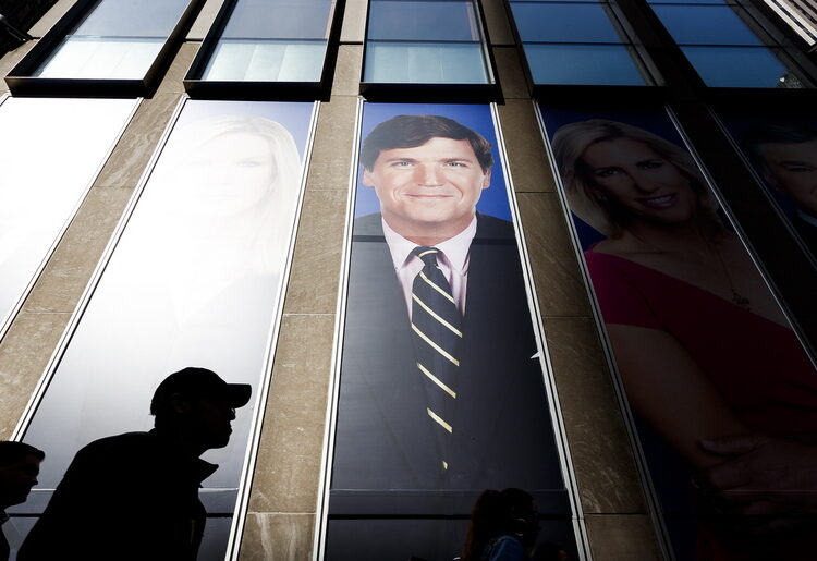 epa07434414 People walk past pictures of Fox News hosts including Tucker Carlson (C) at the studios of Fox News at the News Corporation building in New York, New York, USA, 13 March 2019. Recently compiled recordings of Carlson have lead to widespread allegations that he has regularly used racist and sexist rhetoric. EPA/JUSTIN LANE