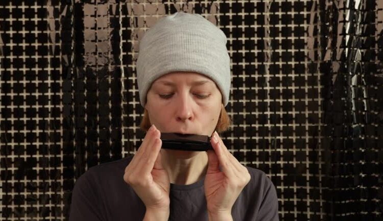 Harmonica lessons, woman playing musical instrument at home, silver harmonica practice in studio setting, leisure activity focused on musical skill.